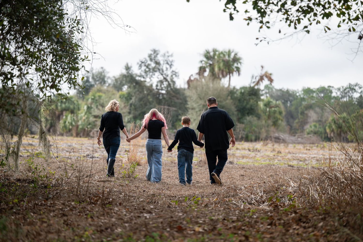 A family walks together down a dirt path surrounded by trees on a misty morning.