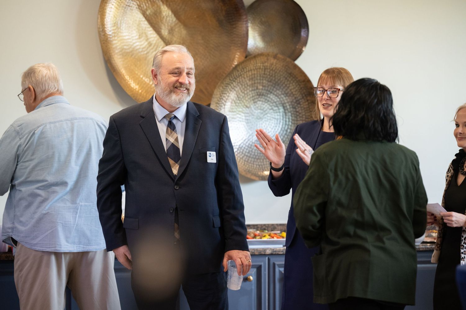 Business professionals engage in animated conversation during a networking event in a bright office space.