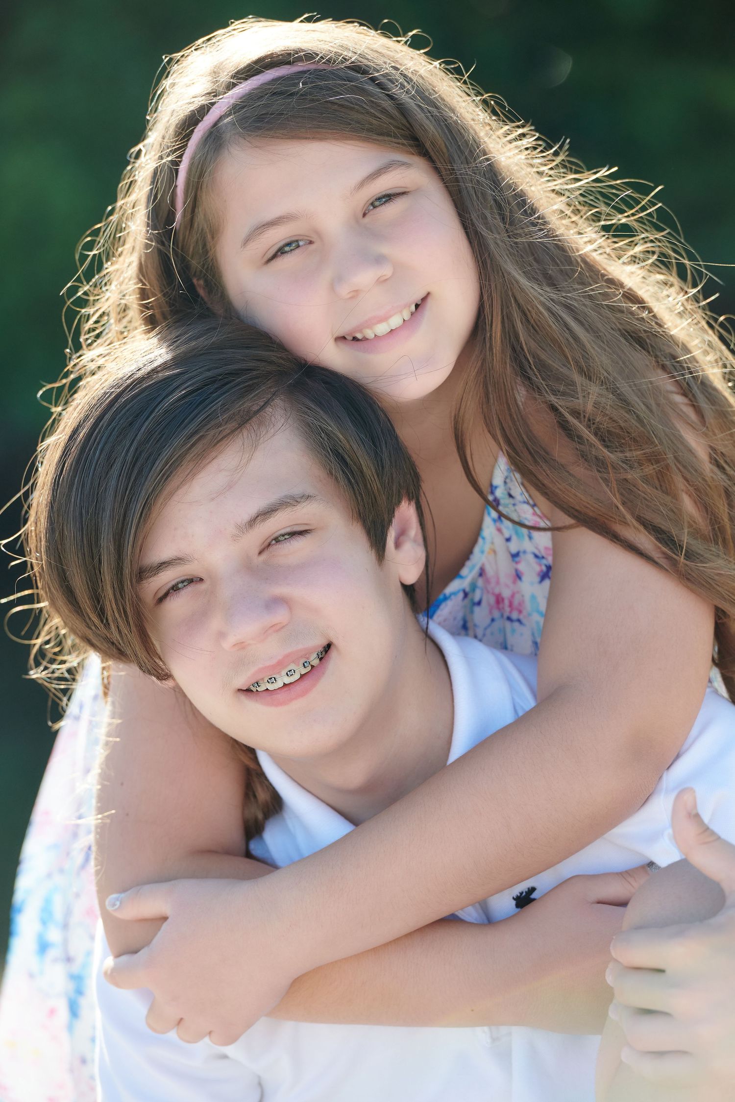 Two children sharing a sweet embrace and laughing together outdoors in natural sunlight.