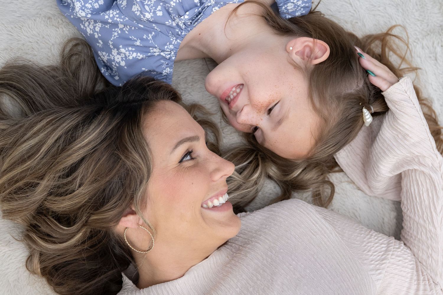 A parent and child lie on the floor together laughing and sharing a joyful moment.