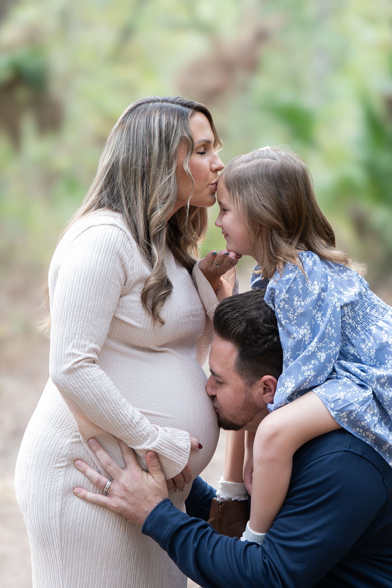 A tender family maternity photo outdoors with parents and child sharing an intimate moment in nature.