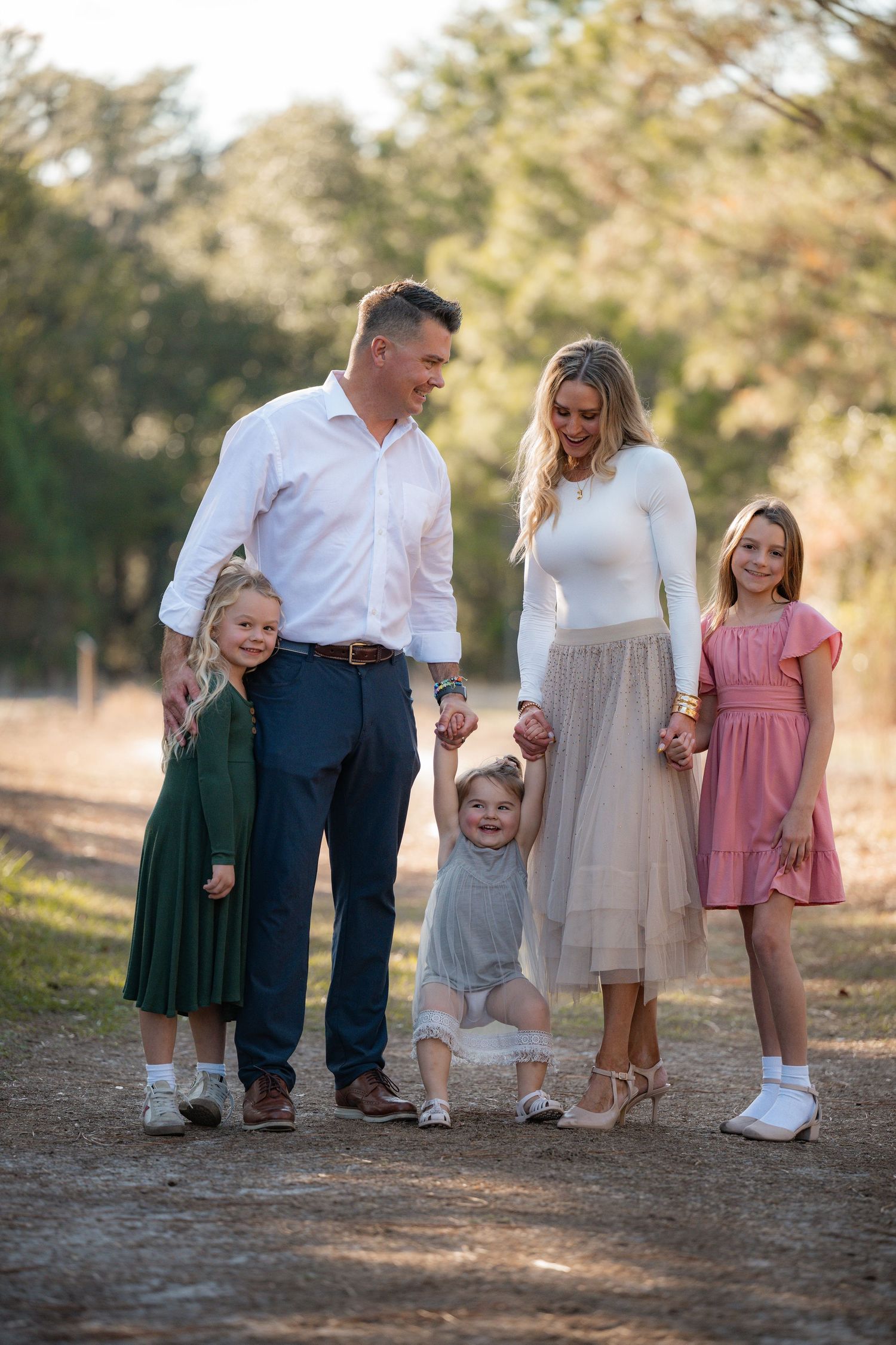 A family of five stands together on a dirt path in casual coordinated outfits during golden hour.