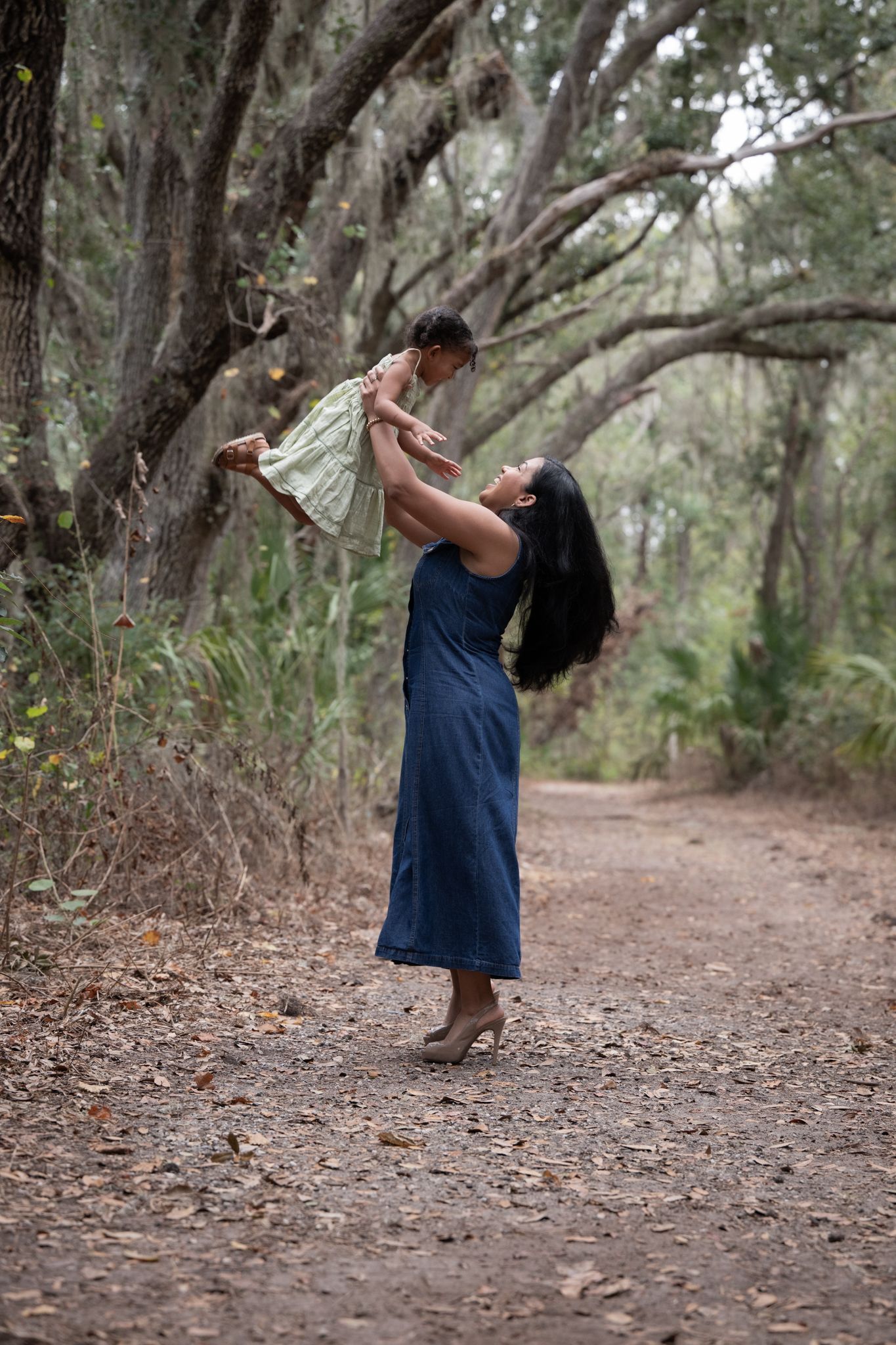 A figure in a blue dress dances and twirls gracefully along a tree-lined dirt path in a natural setting.