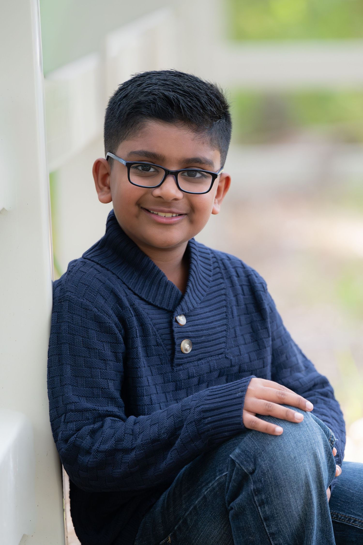 A child in a navy blue sweater sits casually outdoors while smiling at the camera.