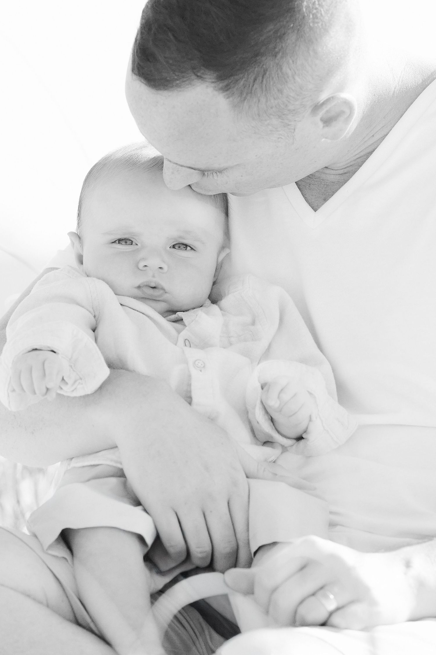 A series of black and white photos showing tender moments between parent and baby in white clothing.