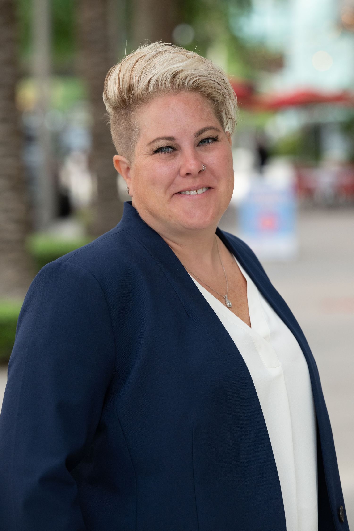 Professional woman with short blonde hair wearing navy blazer smiling outdoors.