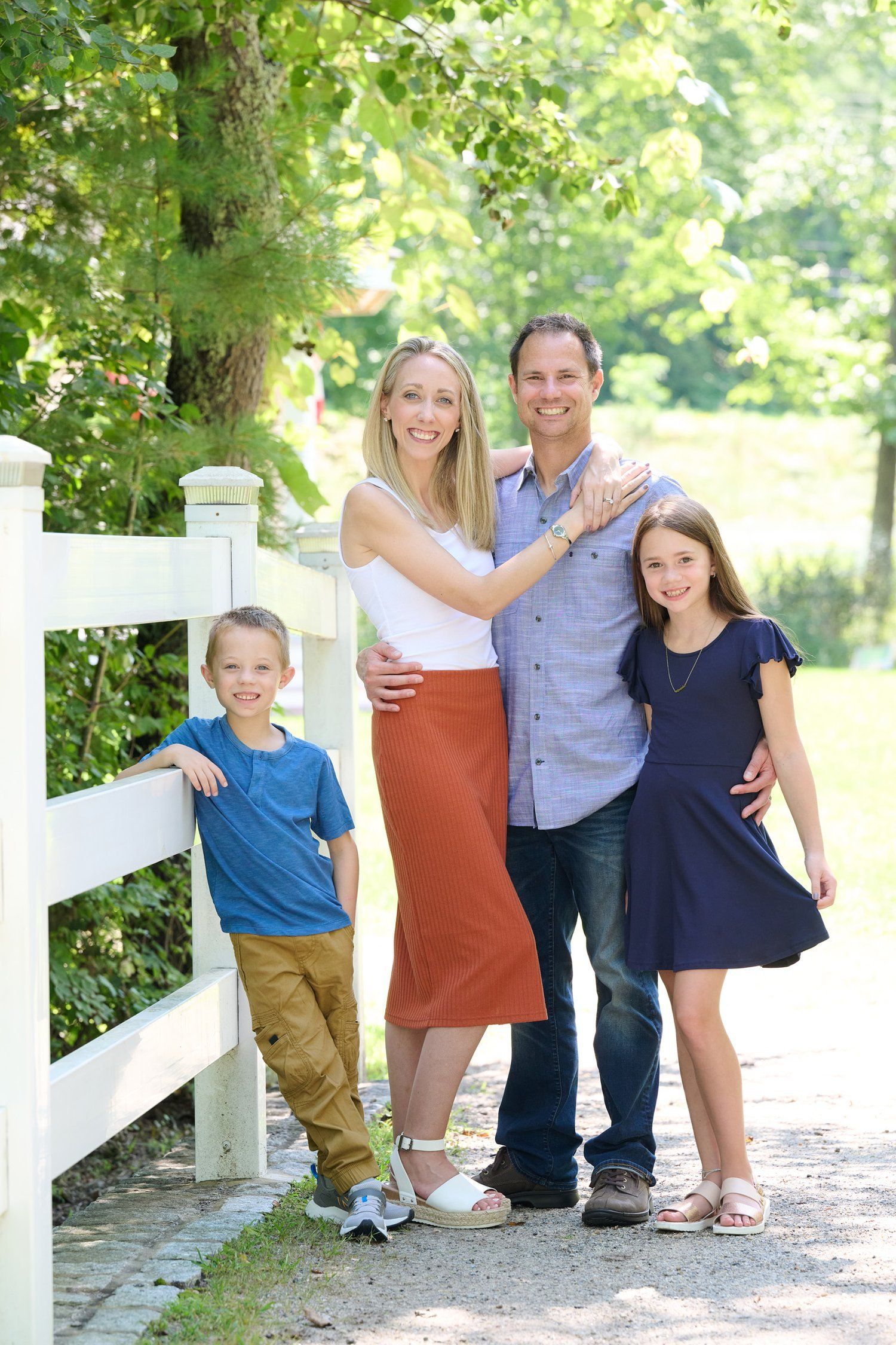A family group sits together on stone steps surrounded by greenery and a white fence.