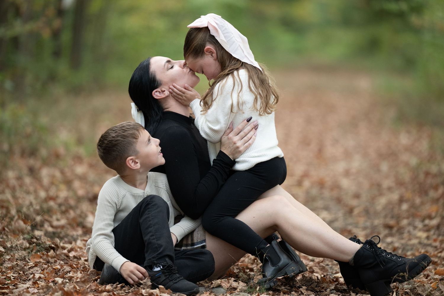 A tender family moment captured outdoors during autumn with fallen leaves scattered on the ground.