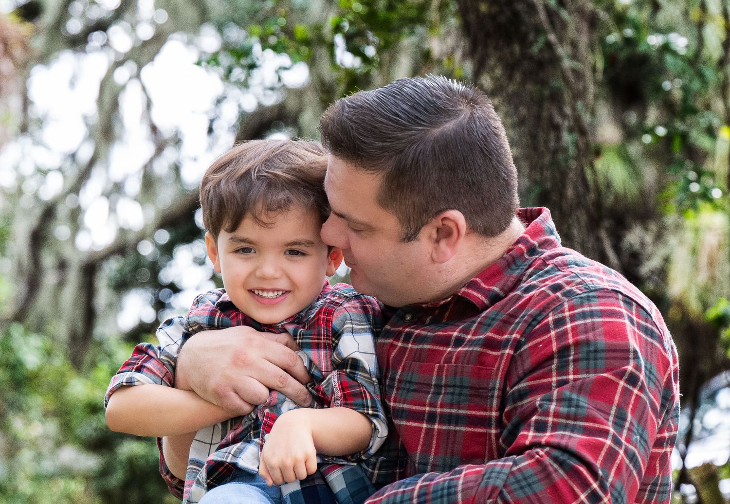 A tender moment shared between parent and child outdoors, both wearing plaid shirts against a natural backdrop.