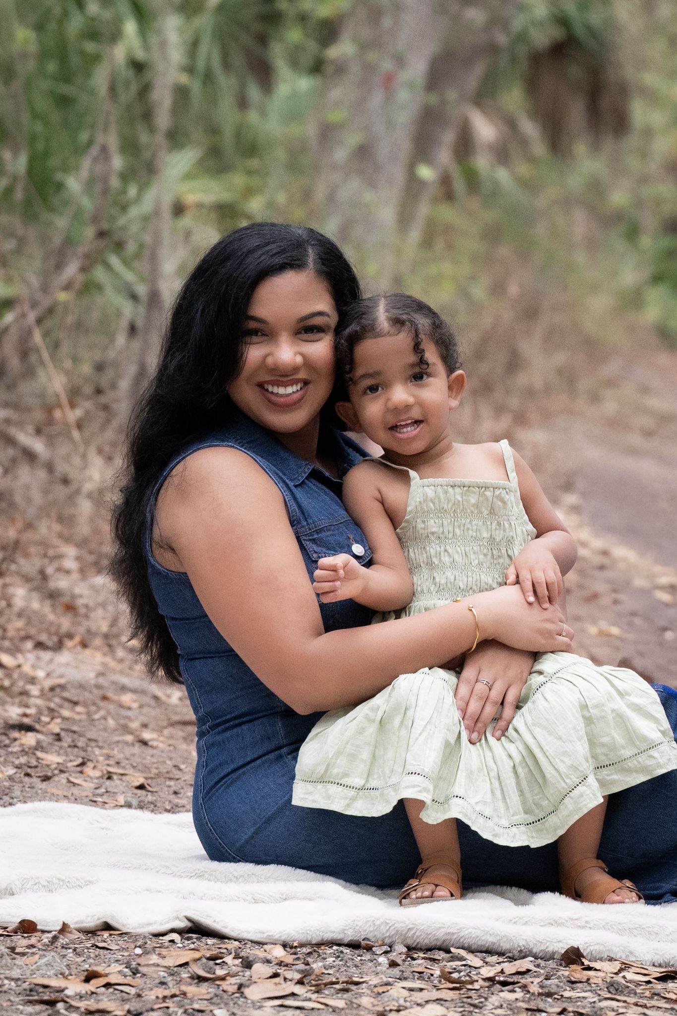 Mother and child share loving moments while sitting on white blanket outdoors for family photos.