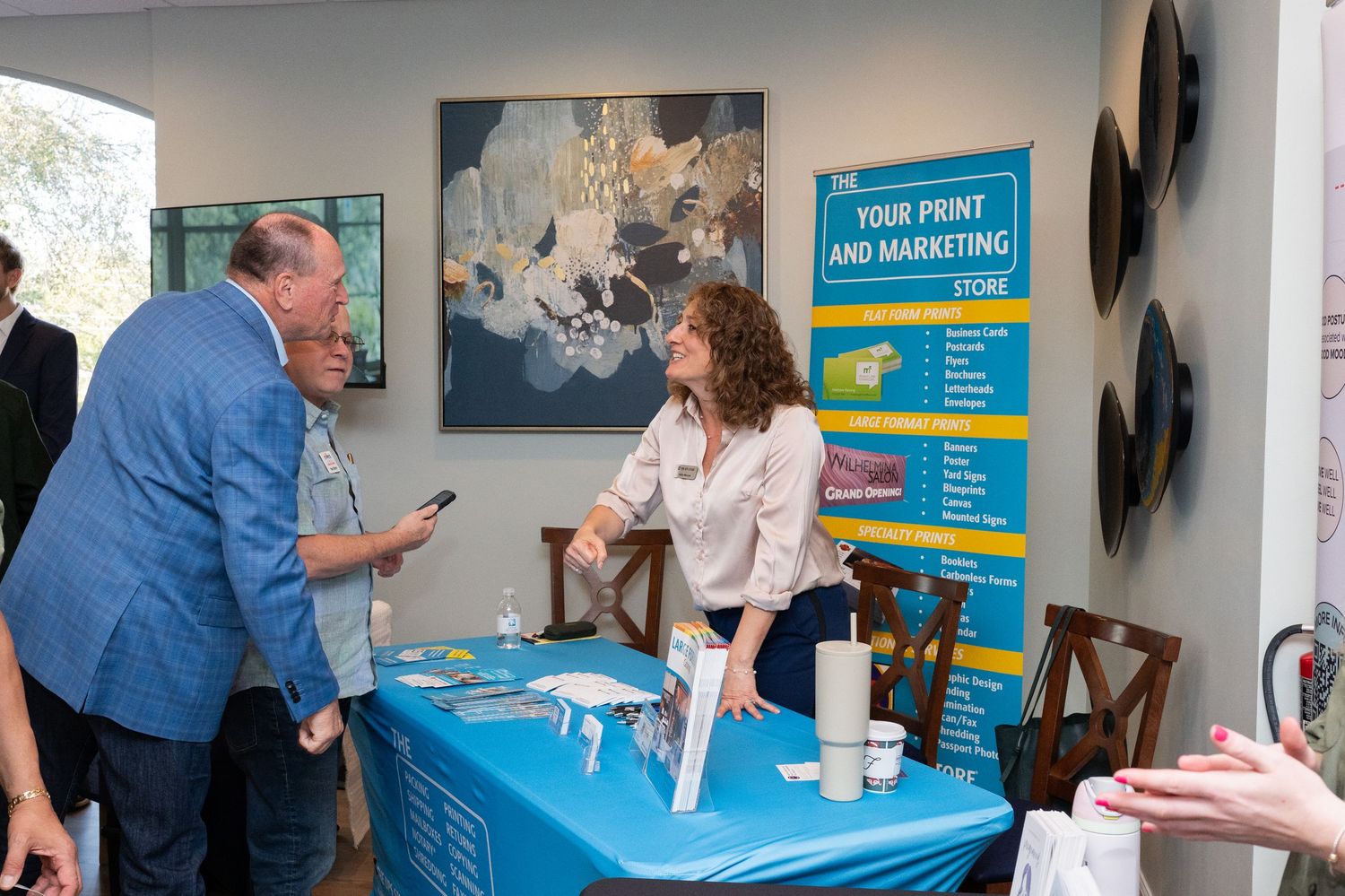 Two people stand at a blue table with informational displays and materials during an event presentation.