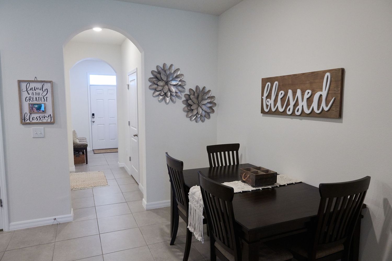 Modern dining room with black chairs, light gray walls, and rustic farmhouse decor including wall art and clock.