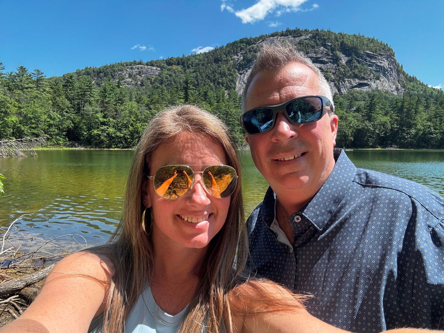 Outdoor selfies taken at a scenic mountain lake with blue skies and forested peaks in the background.