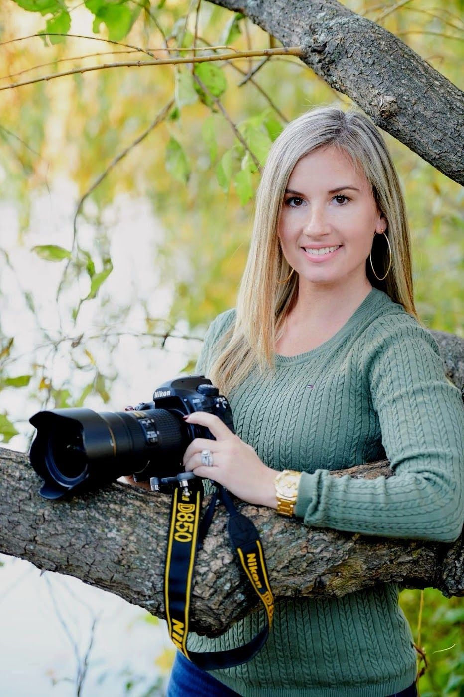 Photographer in a green sweater lying on a tree branch with a professional camera in an autumn setting.