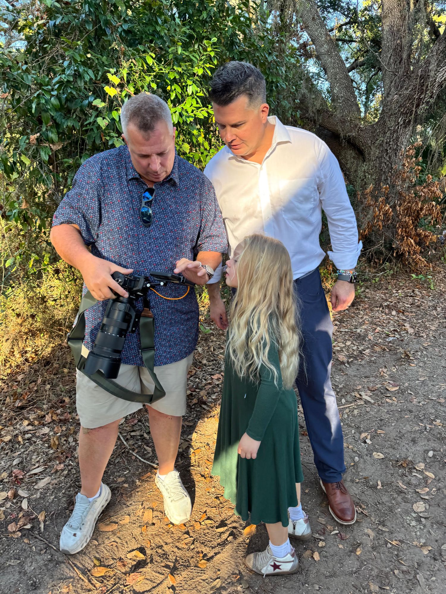 Two people examine a camera together outdoors in a wooded area during golden hour lighting.