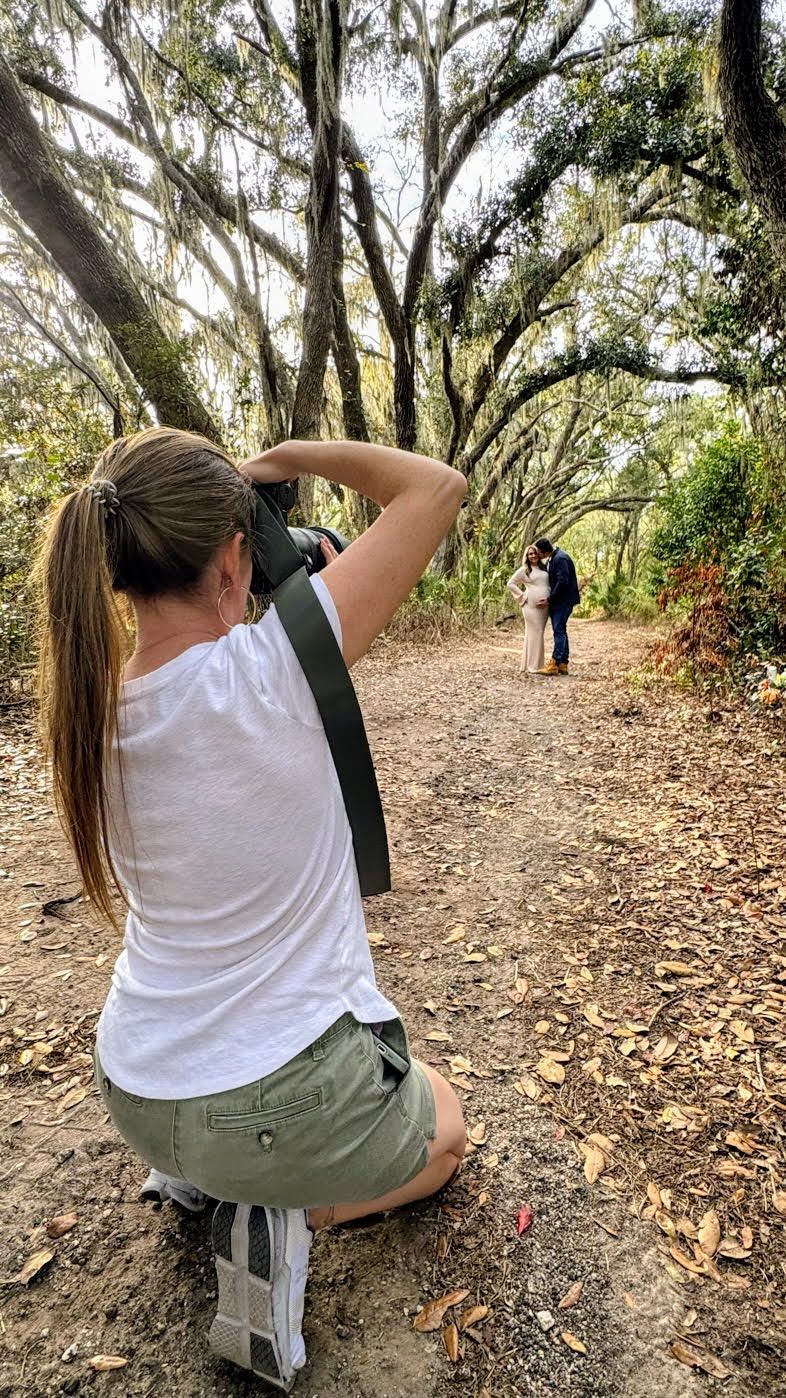 Person in white t-shirt and khaki pants sits on small folding stool while birdwatching on a wooded trail.