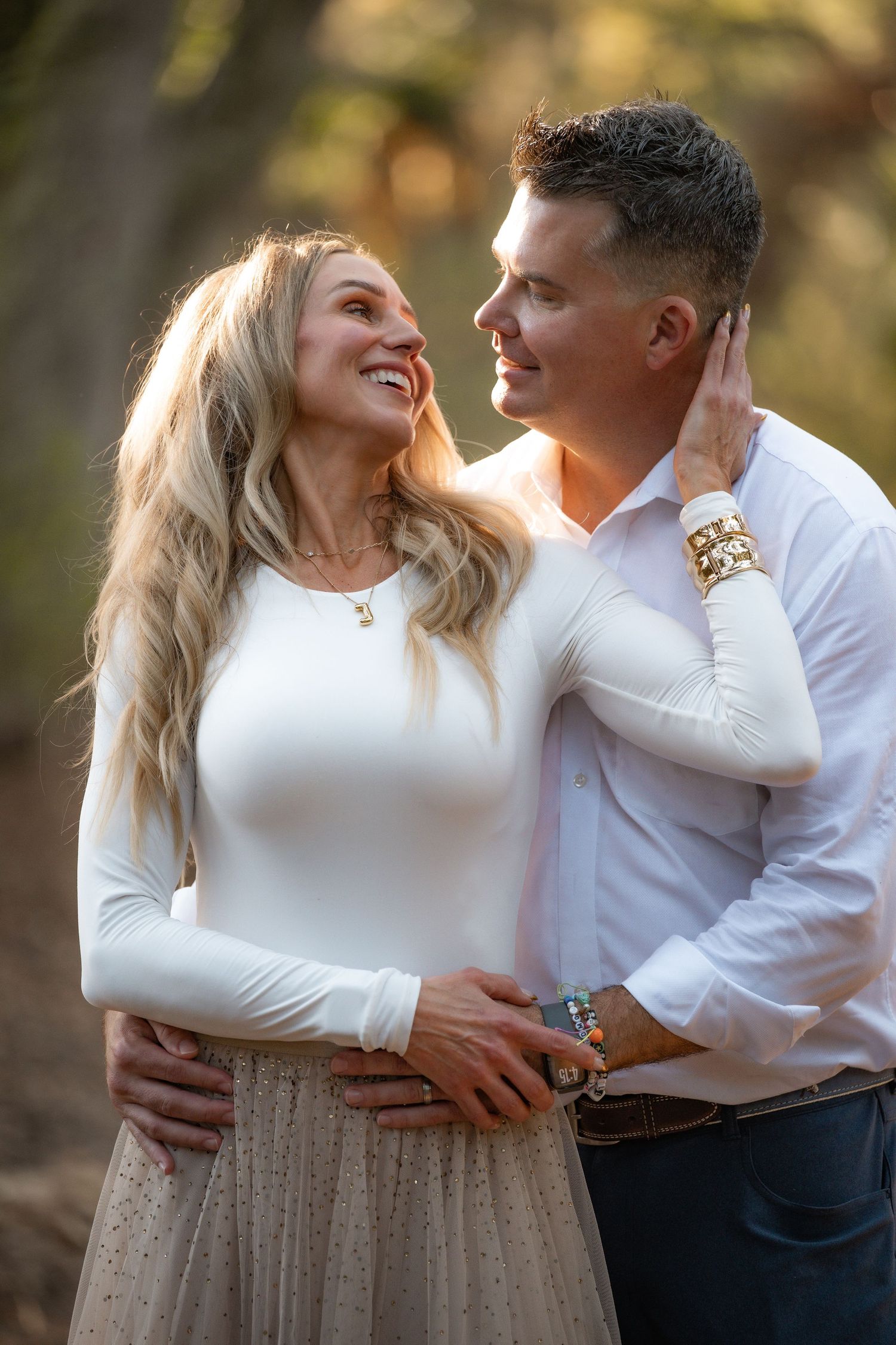 Romantic couple in white outfits embracing and laughing together during an outdoor photo session.