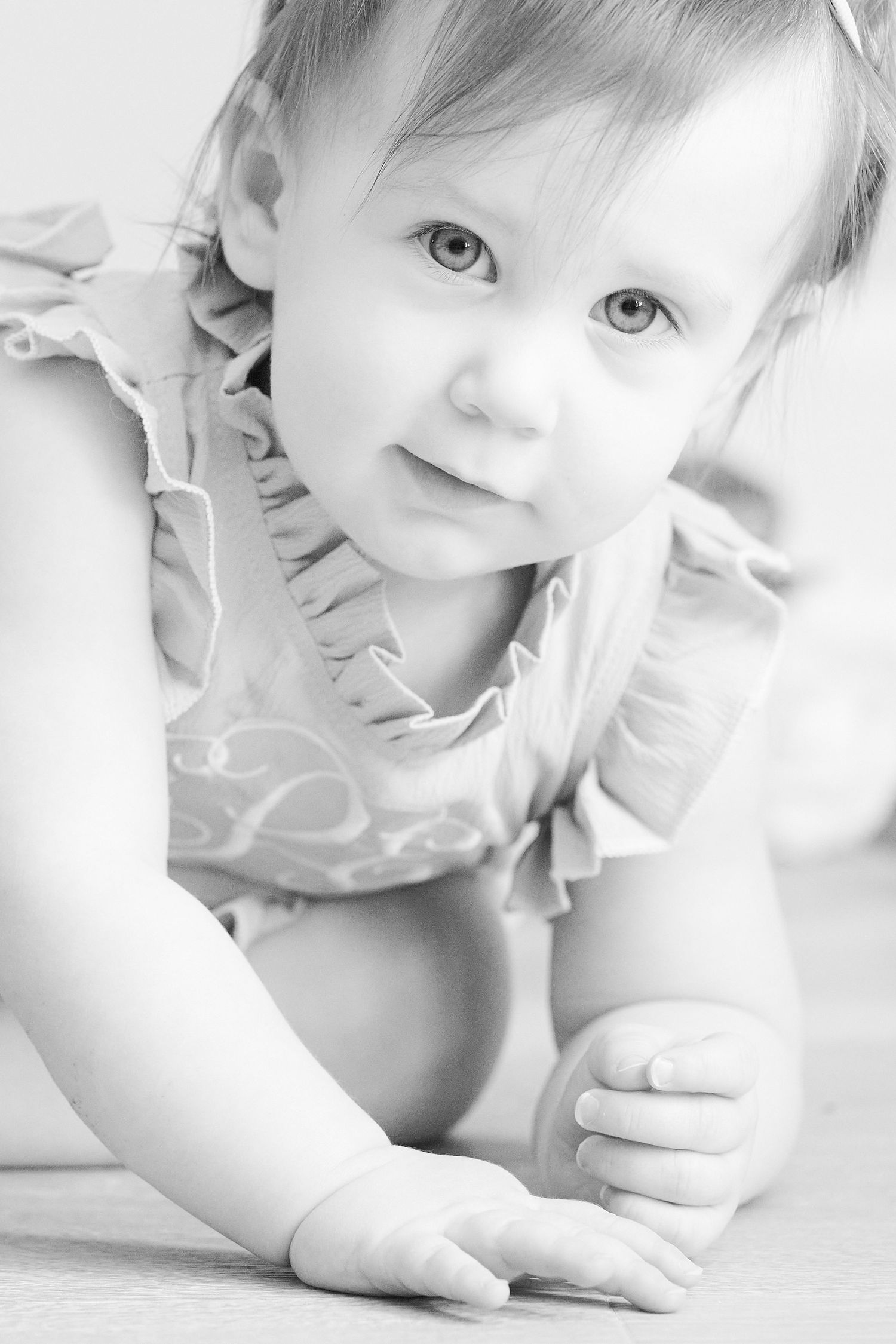 A baby in white ruffled clothing crawls and plays during a bright high-key photo session.