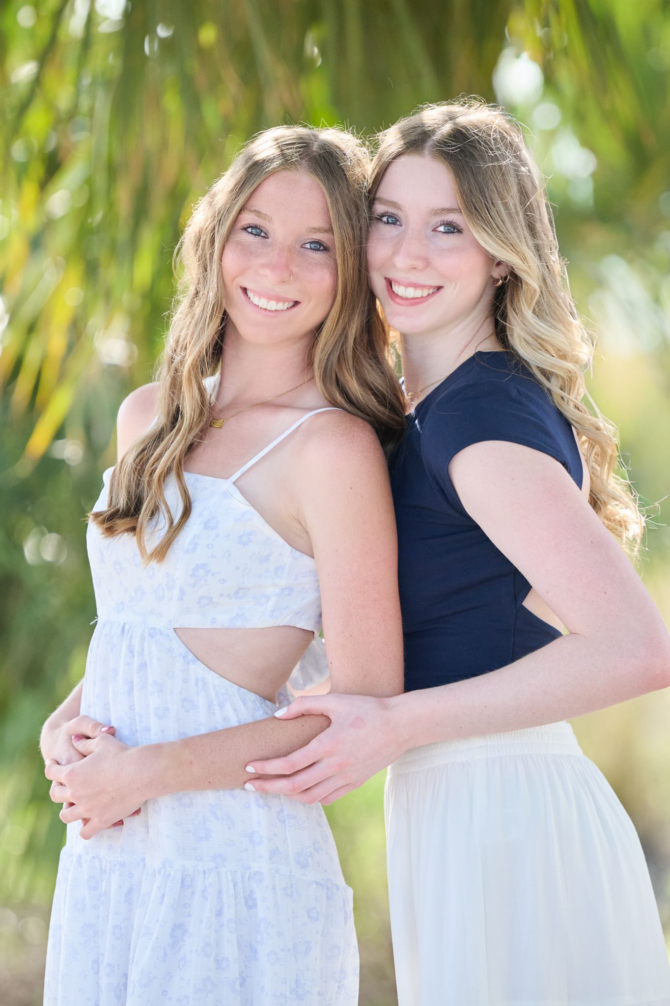 Two friends in white and navy dresses pose together outdoors with palm trees in the background.