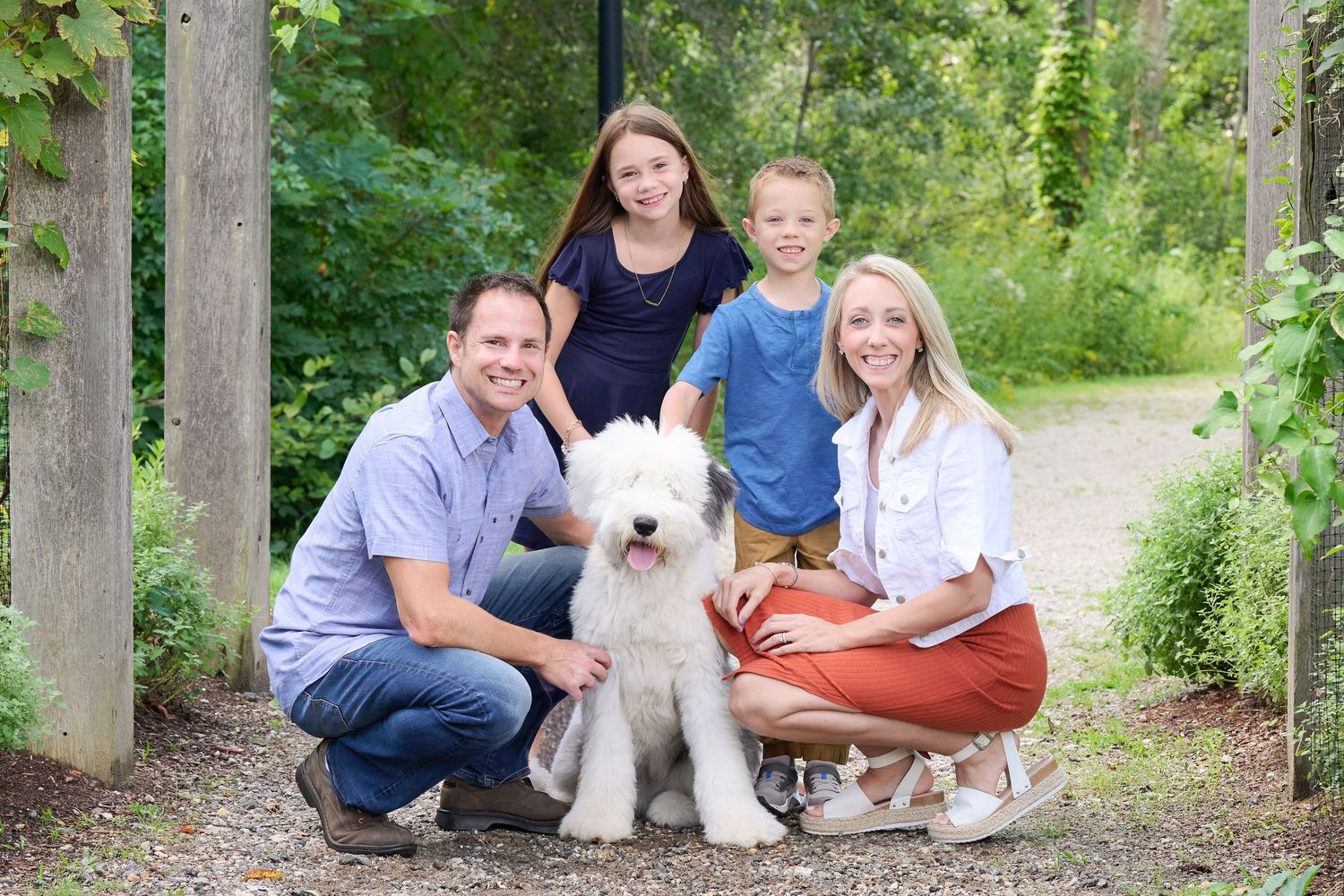 A family and their fluffy white dog pose together on a wooded path during an outdoor photo session.