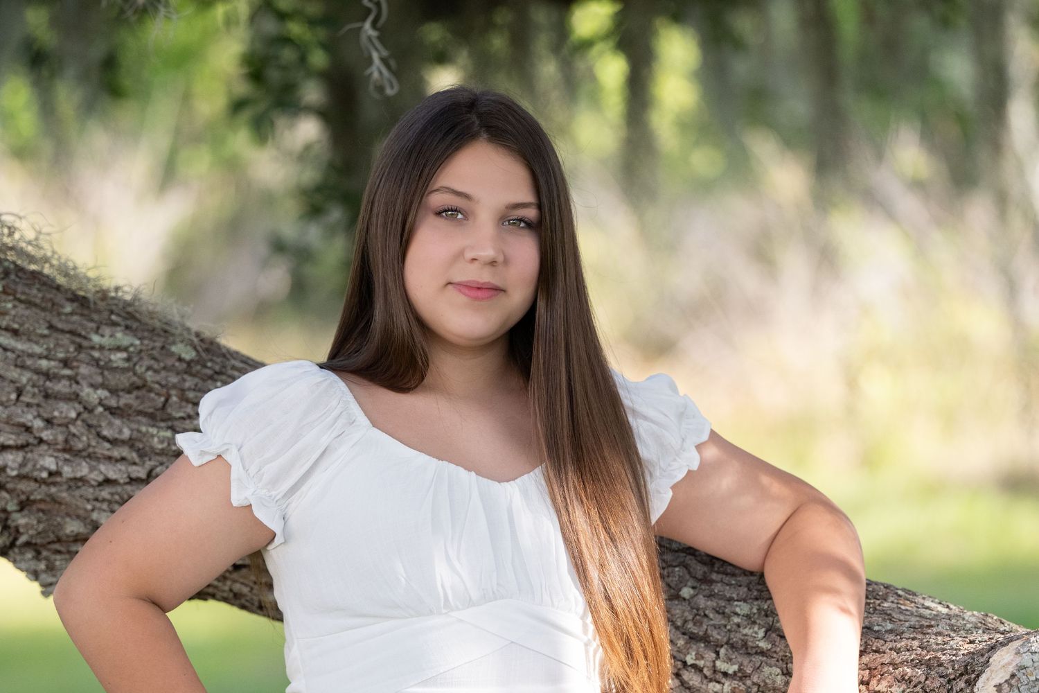 Portrait photography session in a natural outdoor setting with white dress and sunlit background.