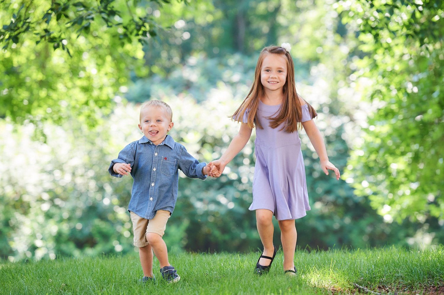 Children play and run together on a grassy hill during a sunny summer day in the park.