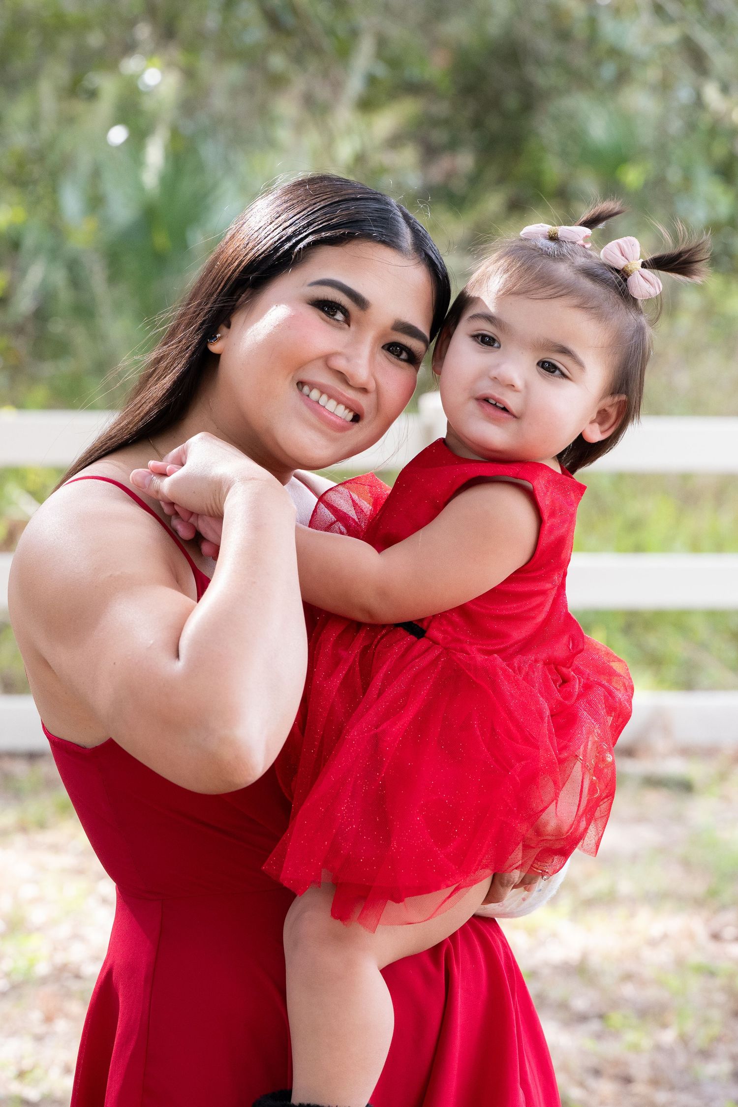 A pair in matching red outfits share joyful embraces and playful poses outdoors in a natural setting.