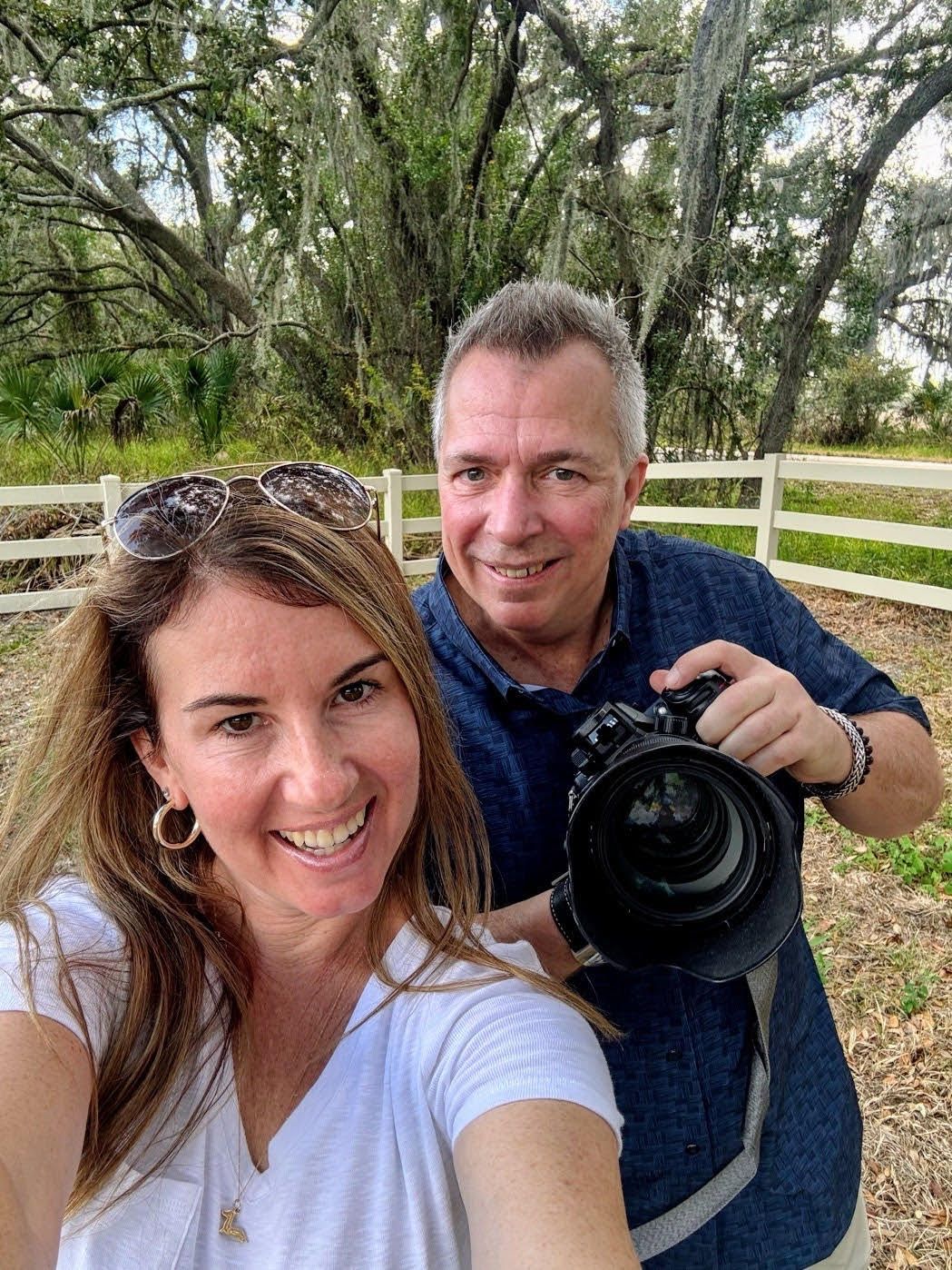 Two people taking outdoor selfies in a wooded area with Spanish moss hanging from trees in the background.