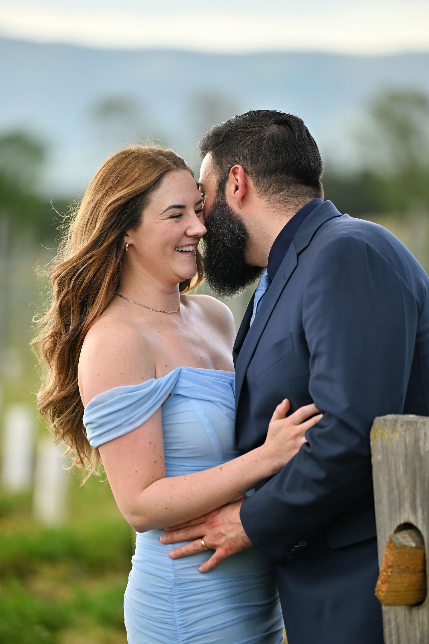 A couple in formal attire share joyful moments together during an outdoor photo session in light blue dress and navy suit.