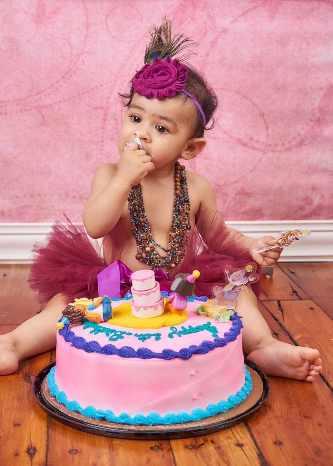 Four sequential photos showing a birthday cake being devoured with pink frosting and colorful decorations on a wooden floor.