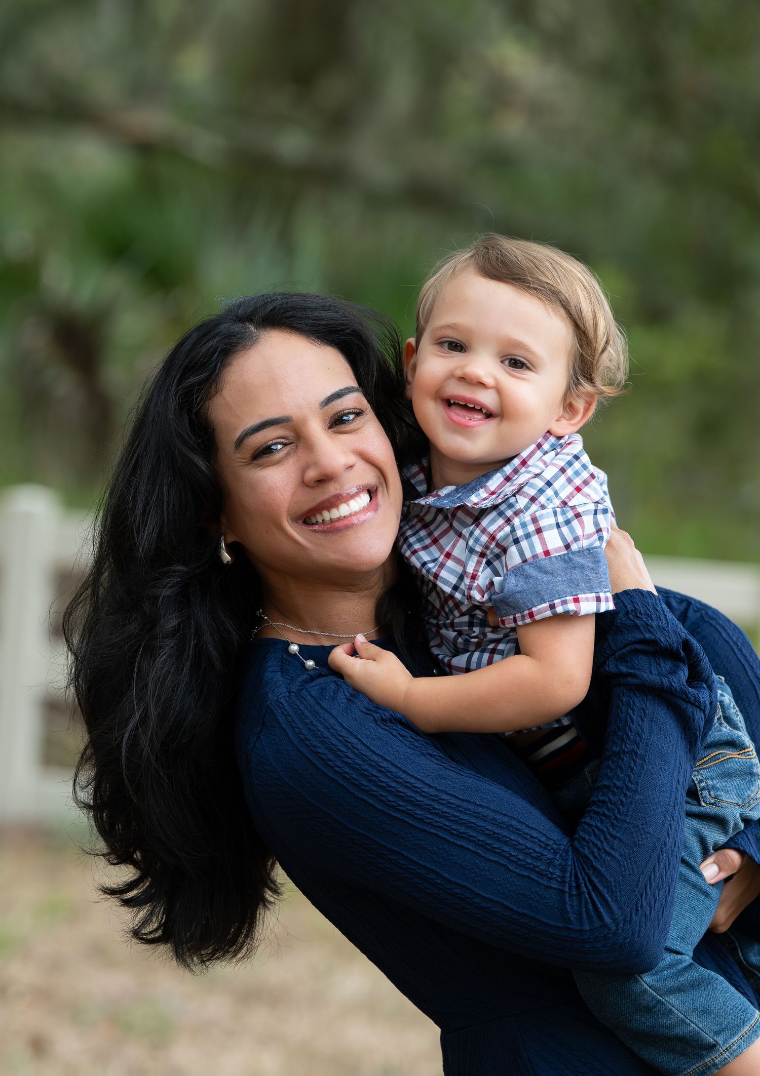 A joyful parent in a navy sweater shares playful moments with a toddler wearing a checkered shirt in an outdoor setting.