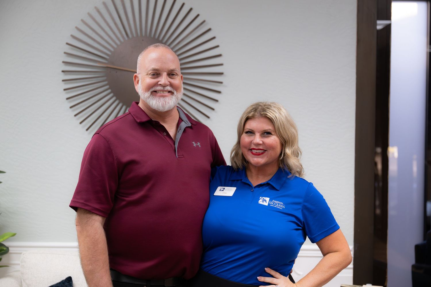 Two people stand together smiling in front of a starburst wall decoration.