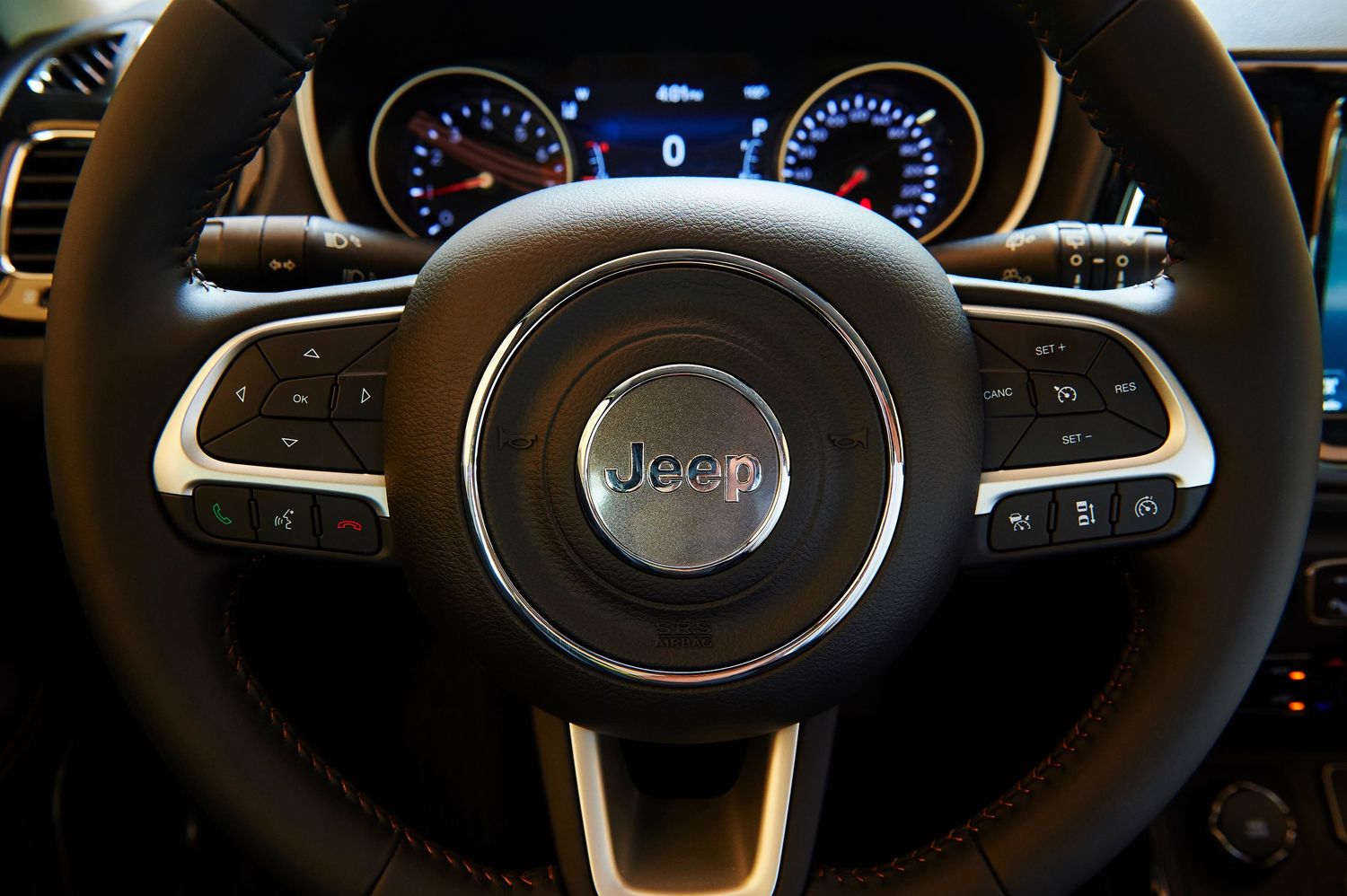 Modern Jeep steering wheel and dashboard controls with blue illuminated gauges.