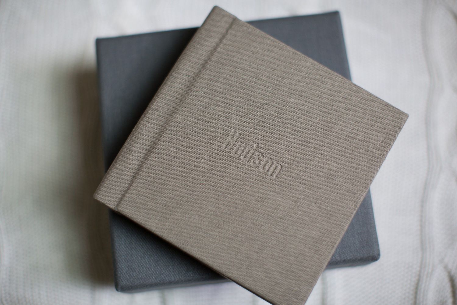 Grey linen fabric covered books or albums arranged in a minimalist style against a light background.