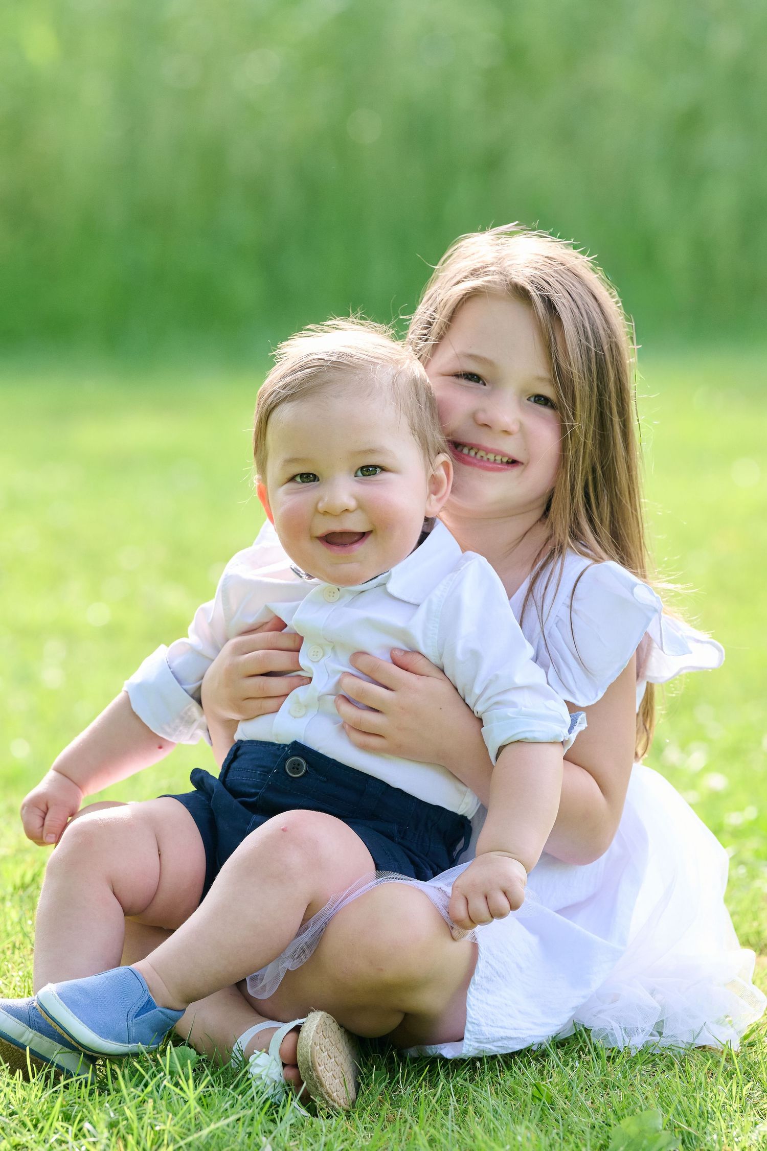 Children sitting together on green grass laughing and playing on a sunny summer day.