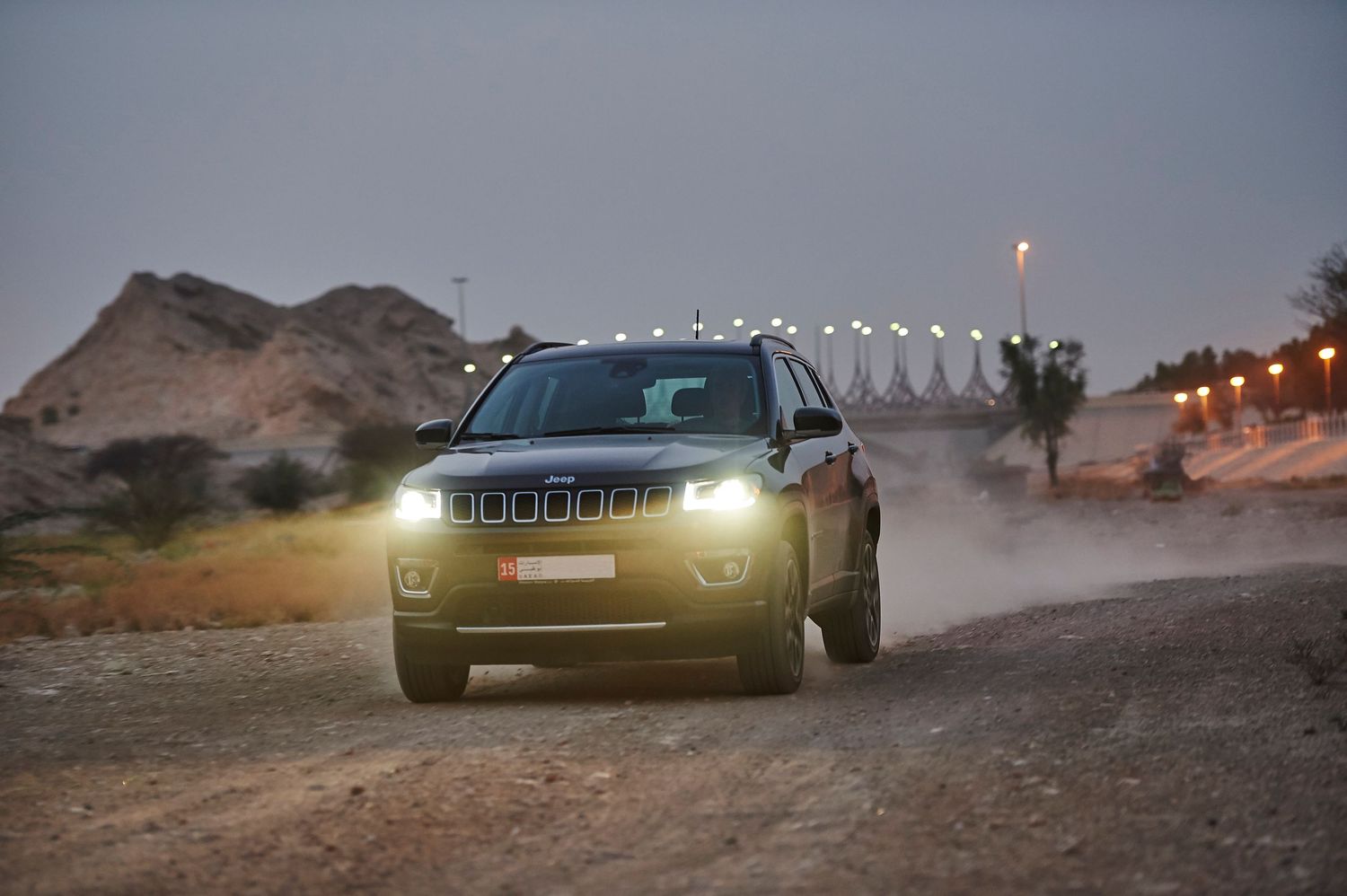 Jeep Compass with bright LED headlights photographed in dark desert environment.