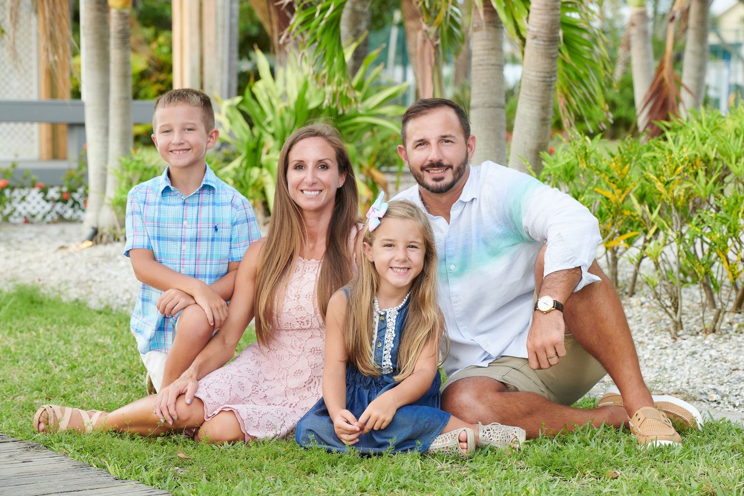 Happy family group lounges together on grass in outdoor garden setting wearing casual summer clothing.