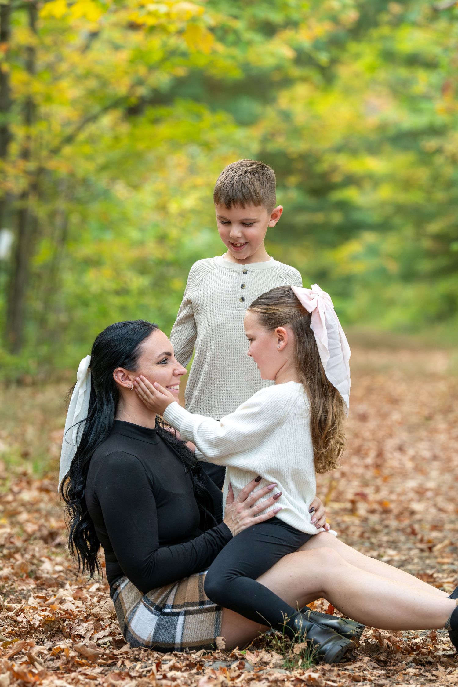 Two people in black and white outfits playfully interact while lying on autumn leaves in a park setting.