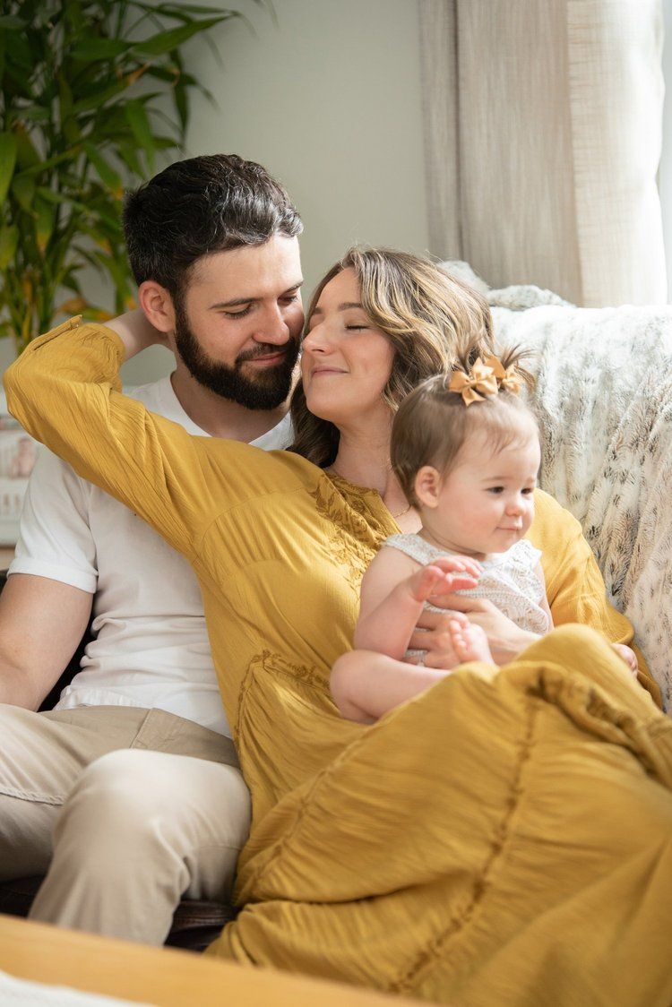 A family shares tender moments together while relaxing on a couch with a yellow blanket in a sunlit room.