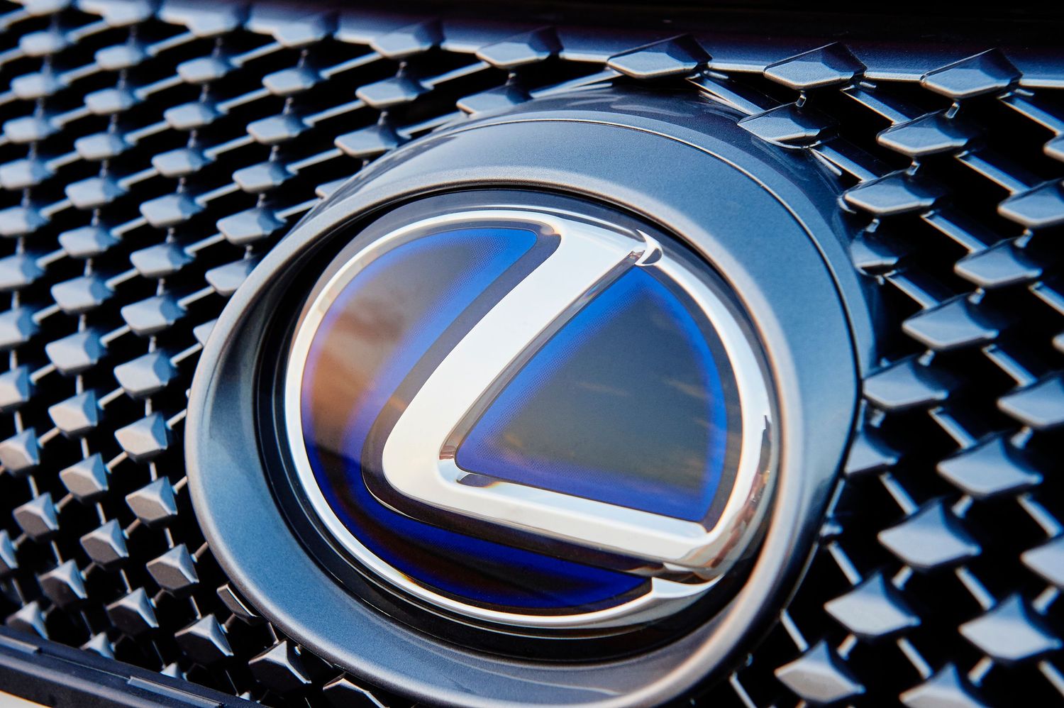Close-up details of Lexus logo and grille pattern showing metallic finish.