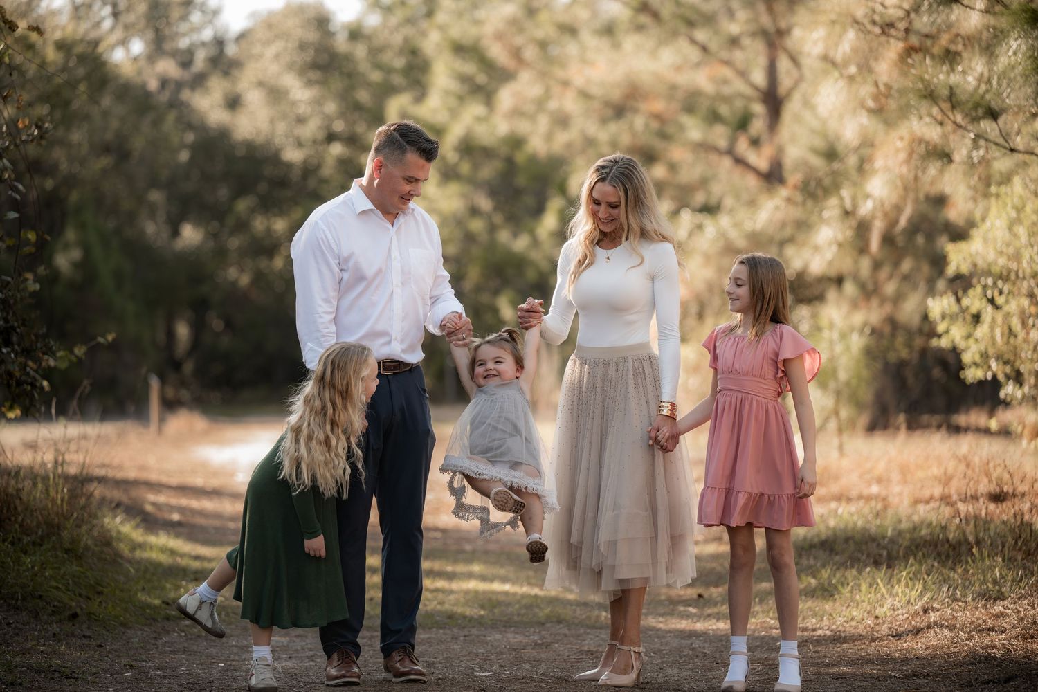 Family walking together on a sunlit path through nature wearing coordinated white and neutral outfits.