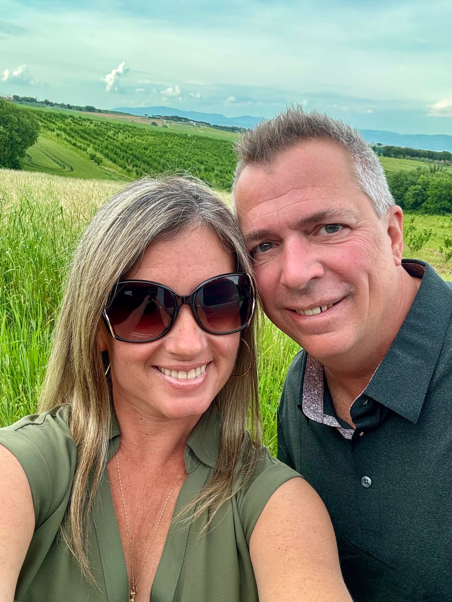 A couple takes a series of selfies together in a green countryside field on a sunny summer day.