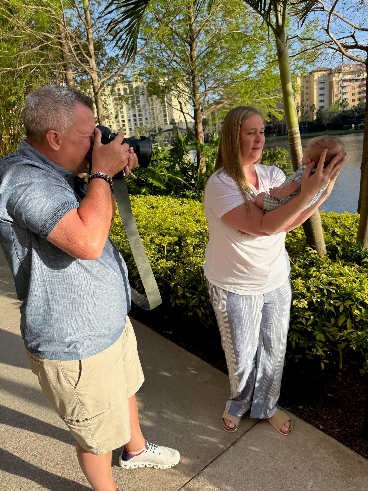 People taking photos with cameras in a sunny garden setting with green bushes and trees in the background.