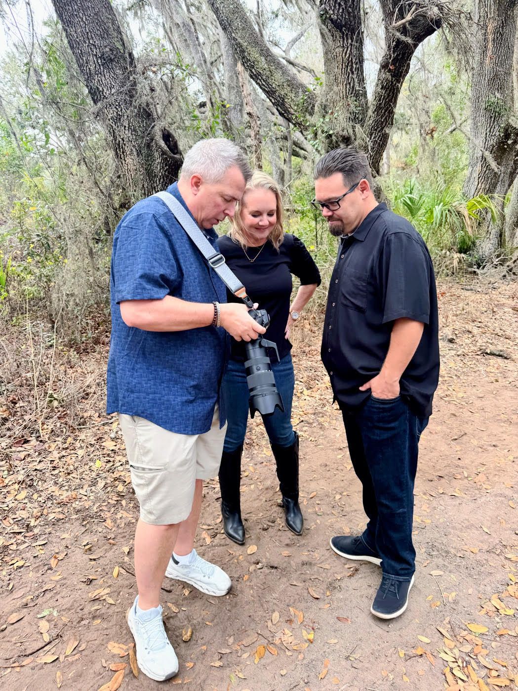 A group of people laughing and sharing a lighthearted moment together on a dirt path surrounded by trees.