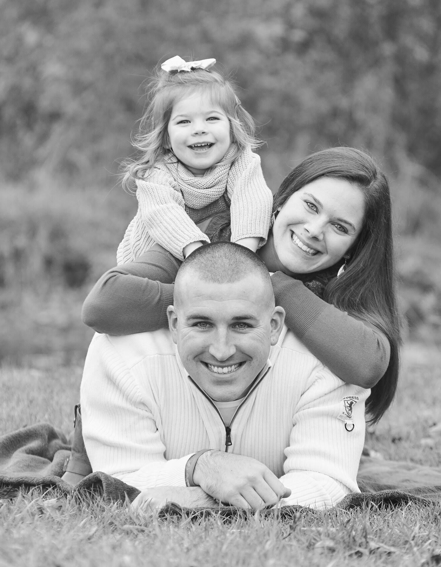 A black and white photo sequence showing a family lying in grass, playing and laughing together outdoors.