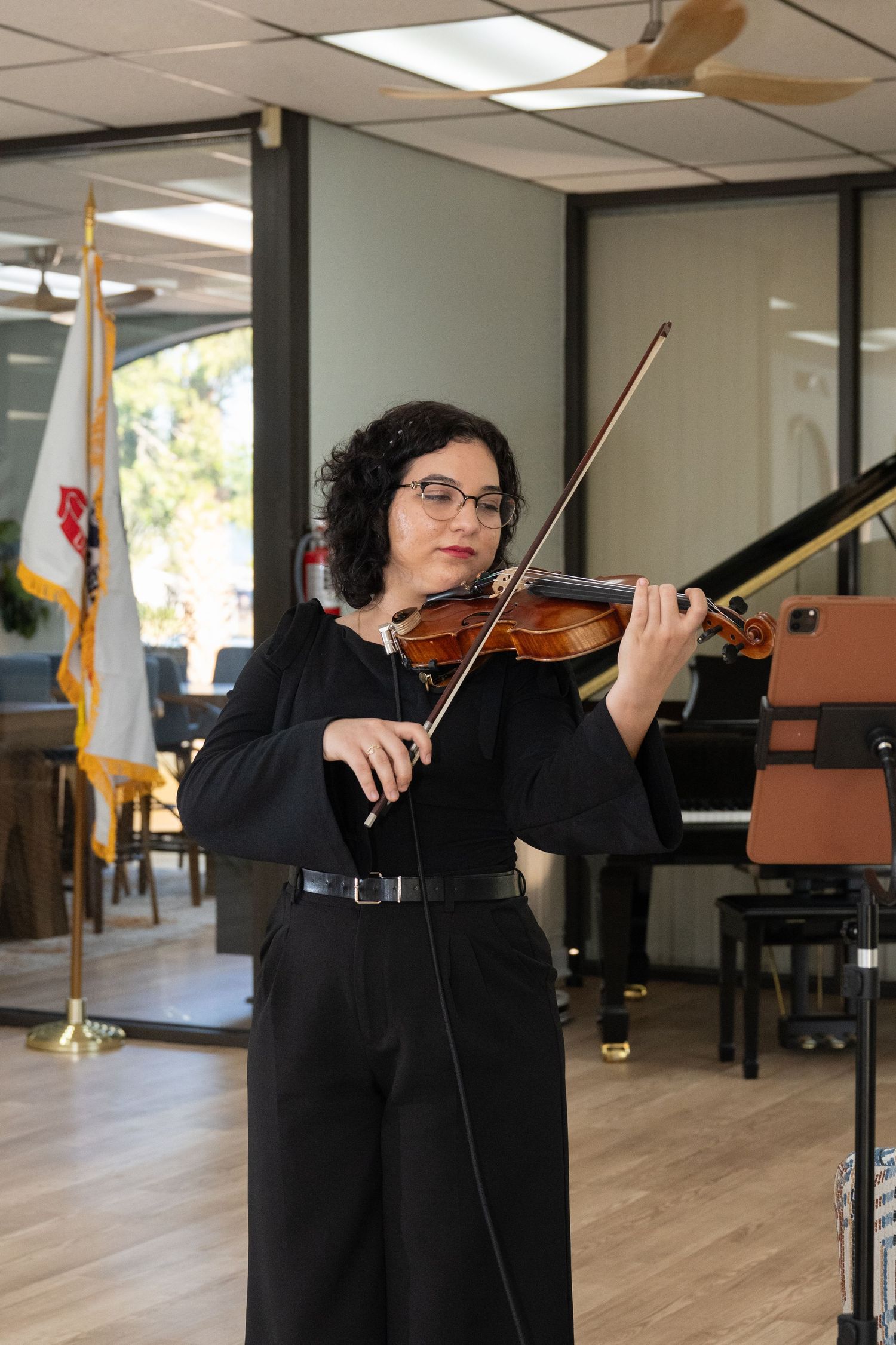 Musician performing on violin in a studio space with pianos and musical equipment.