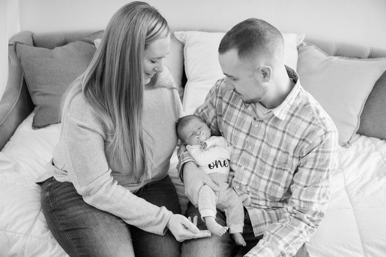 A family sits together on a couch, sharing a tender moment with their baby in black and white photography.