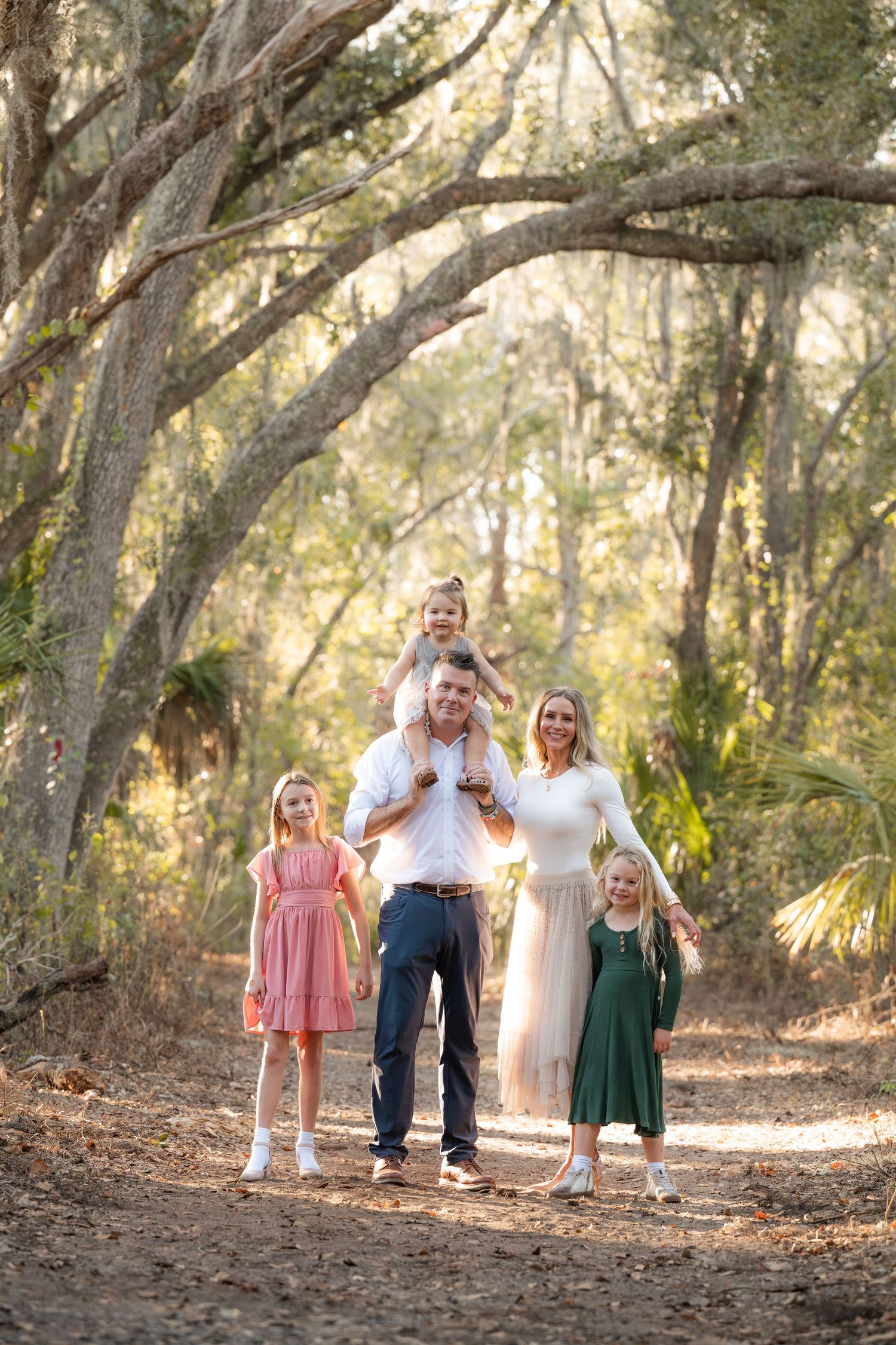 A group walks together on a leaf-covered path through sun-dappled woods during golden hour.