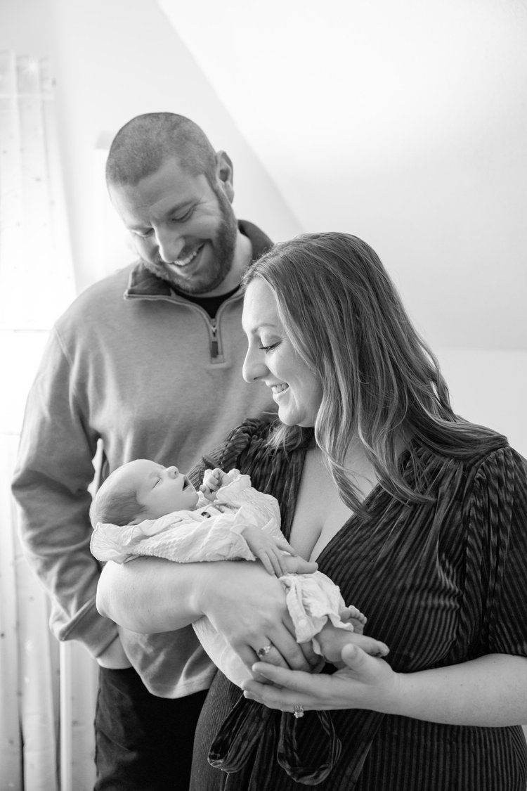 Black and white photos of parents lovingly holding and gazing at their newborn baby in an intimate home setting.