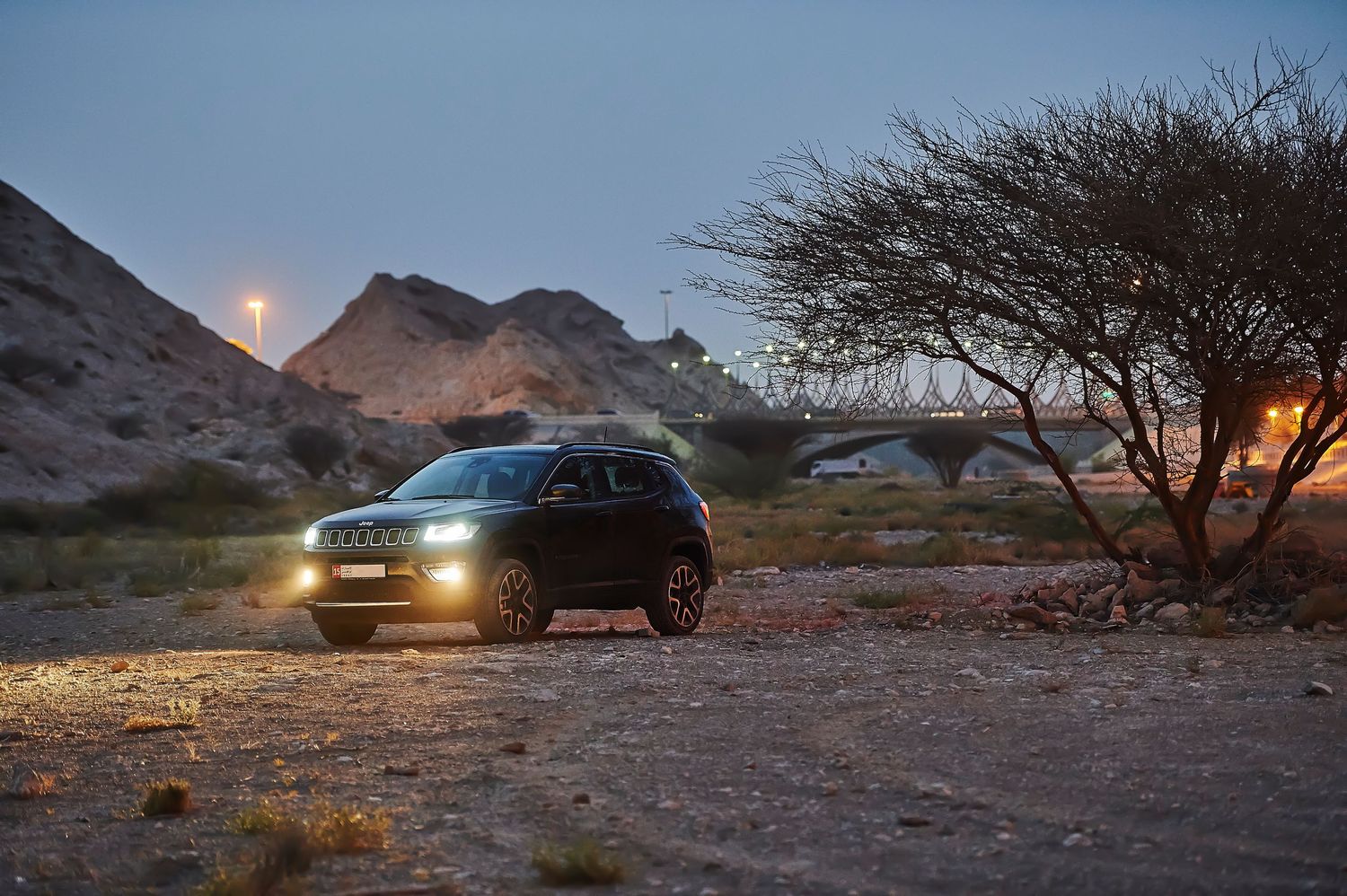 Jeep Compass photographed at dusk in desert setting with headlights illuminated.